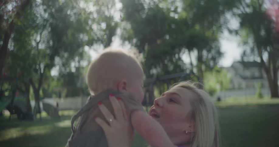 A child is lifted up by his mother on the grass in a park