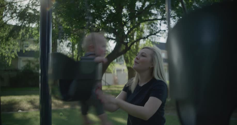 Mother in a park happily swinging her baby son on a swing