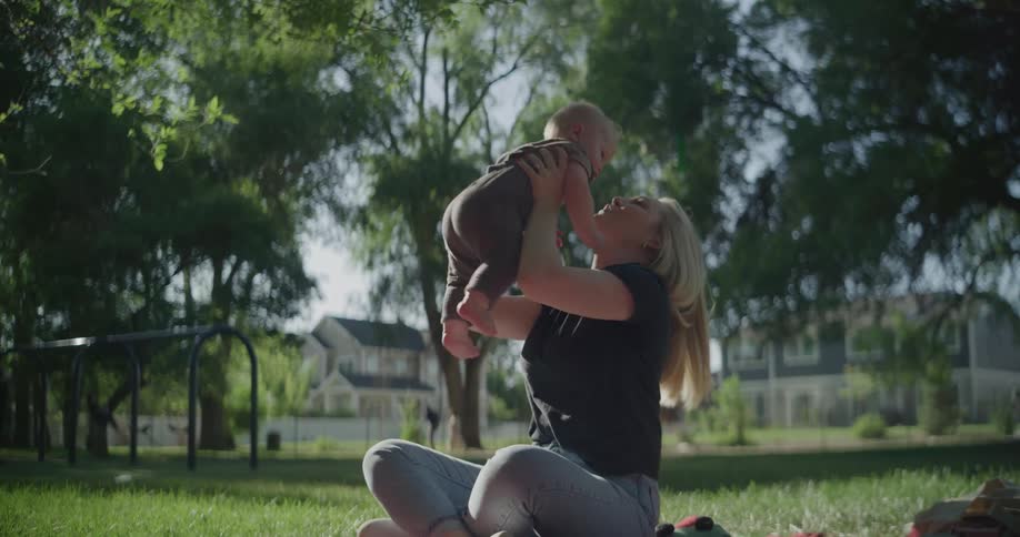 A child is lifted up by his mother on the grass in a park