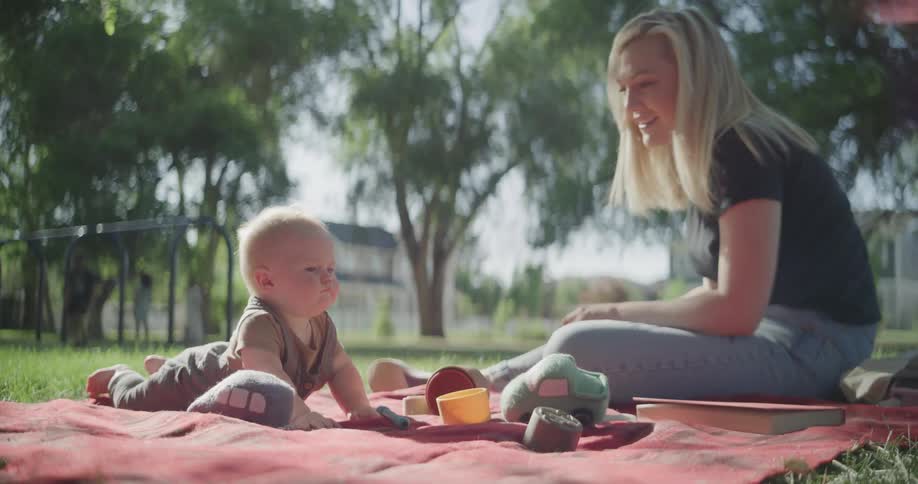 A baby crawls on a grasscovered towel in a park