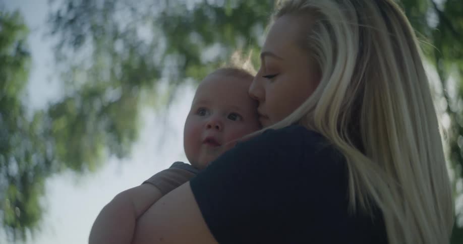 A woman holding her baby outdoor surrounded by trees