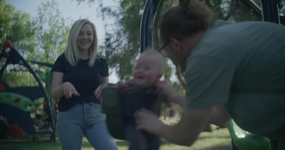 Mother and father push their baby on a swing at the playground