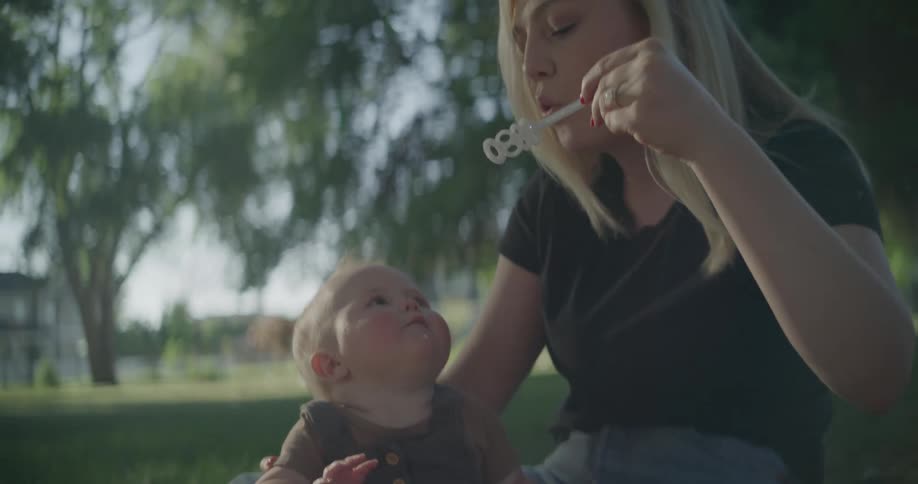 Mother sitting with her son in a garden playing with soap bubbles