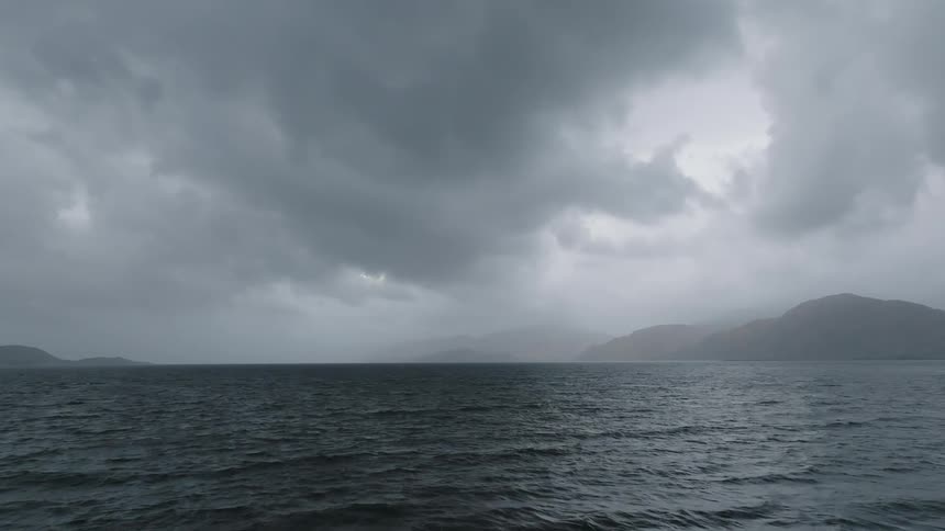 A stormy sky and a dark sea with mountains in the mist