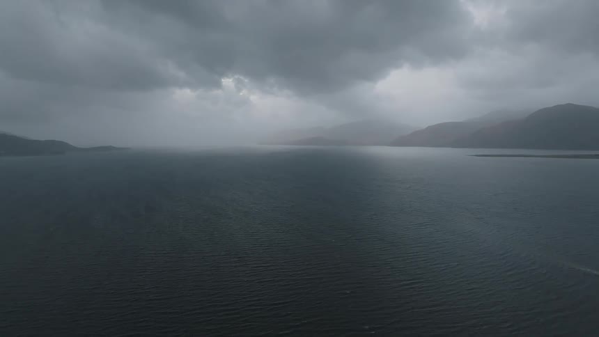 Beneath a cloudy sky there is a large body of water lined with mountains