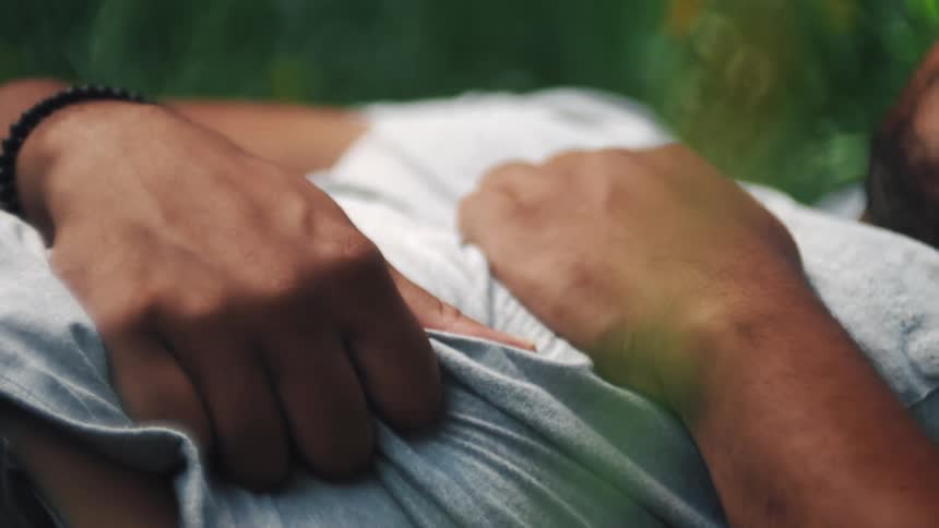 Closeup of a mans hands squeezing his abdomen while lying in the woods