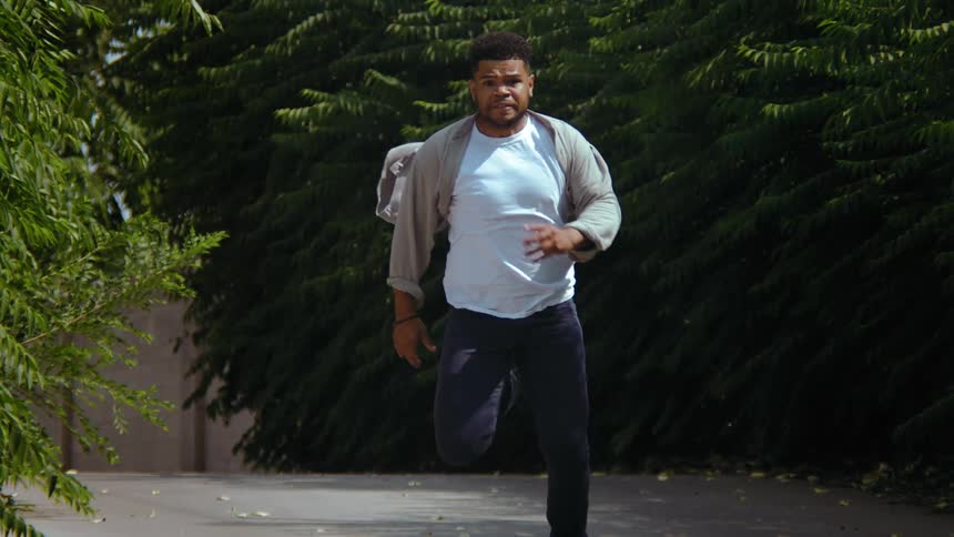 A man wearing street clothes runs as fast as he can along a paved path