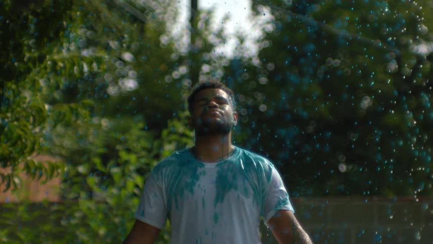 Young man with eyes closed in an outdoor environment with blue paint rain falling beneath him