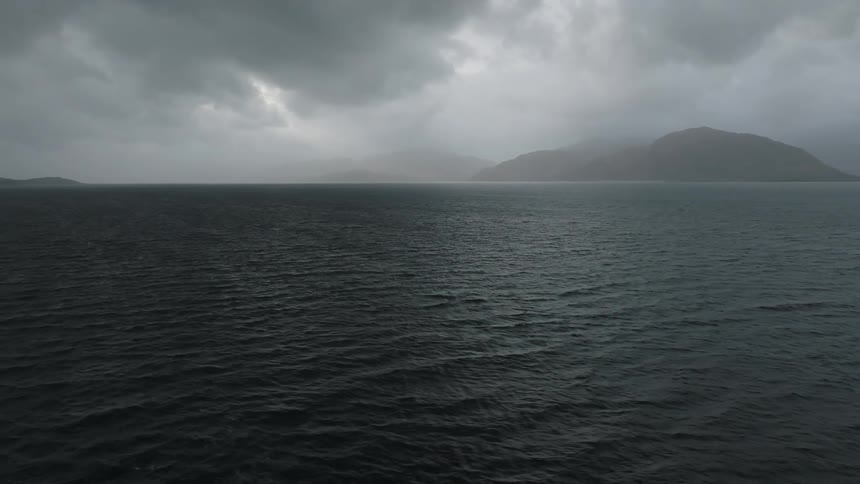 Landscape of a dark ocean with mountains on the horizon on a cloudy day