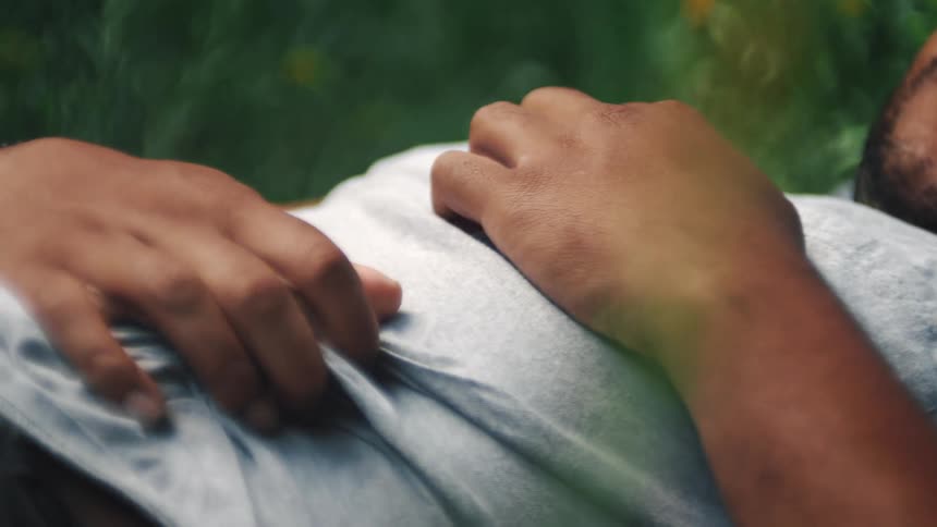Man lying on his back among wildflowers moves his hands across his belly