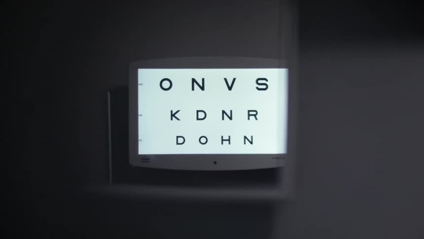 A small screen mounted on a wall displays a vision test with letters