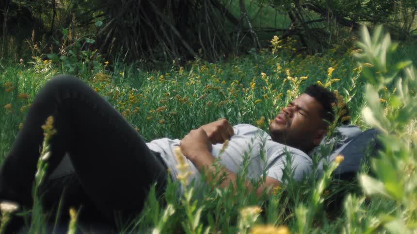 Man lying in a garden sleeping and pressing his hands over his abdomen