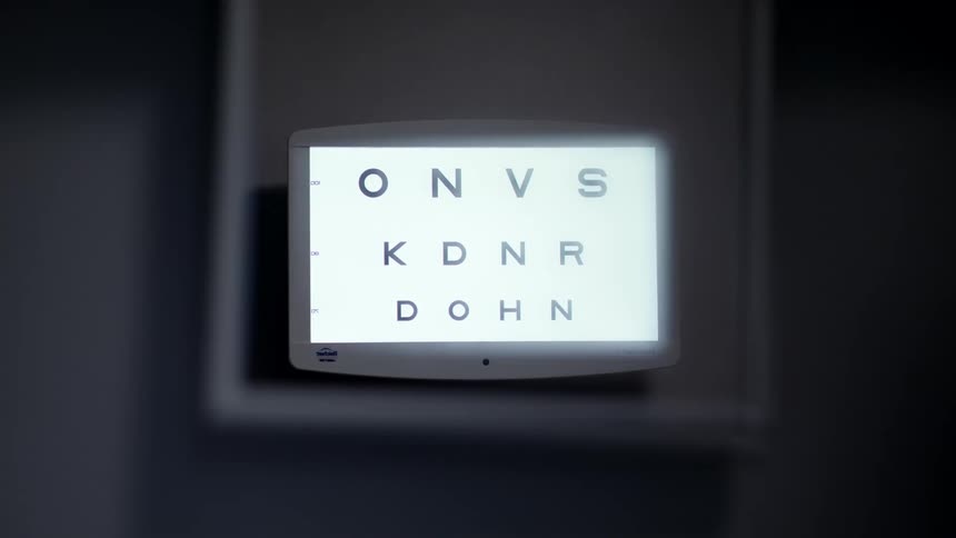 A digital screen shows an eye chart with letters of different sizes in a dark room
