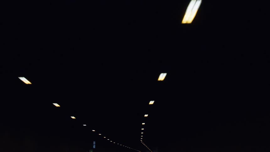Rows of lights on the ceiling of a subway tunnel passing by from a rear perspective
