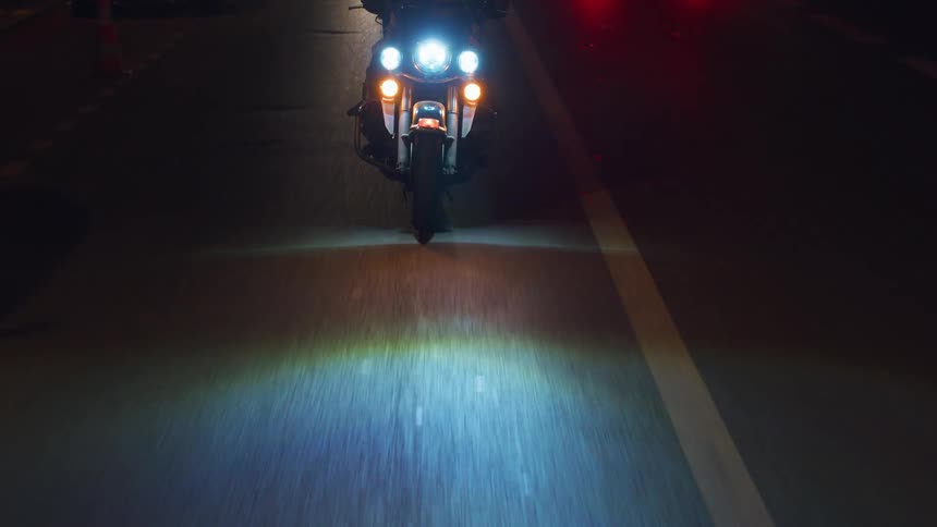 A motorcycle with illuminated headlights is on a road at night