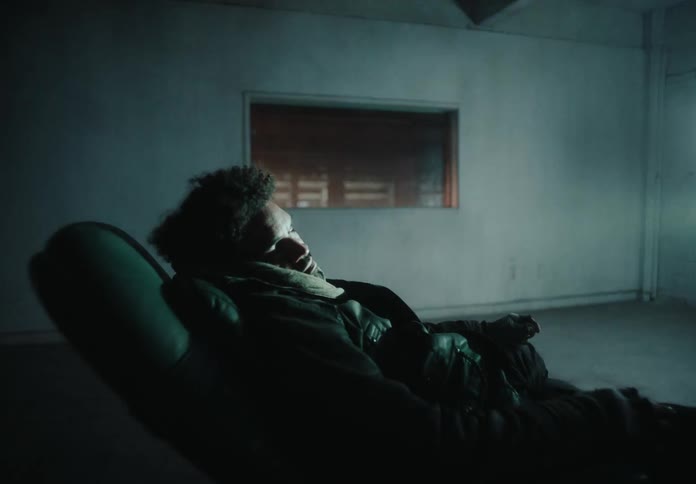 A man sitting on his couch while holding a remote staring at a tv scrren at night alone