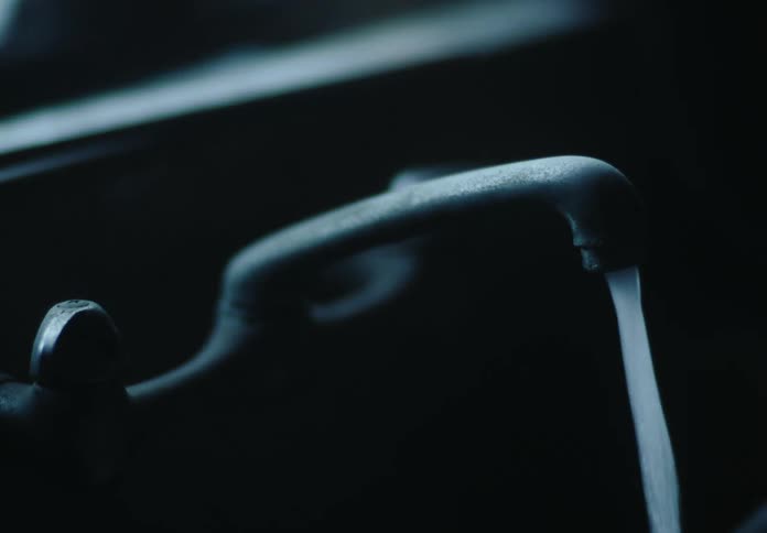 A persons hand opening and closing a tap in a lowlight environment