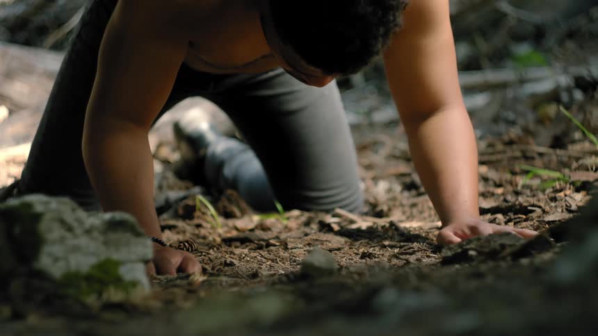 A man kneels down in the dirt