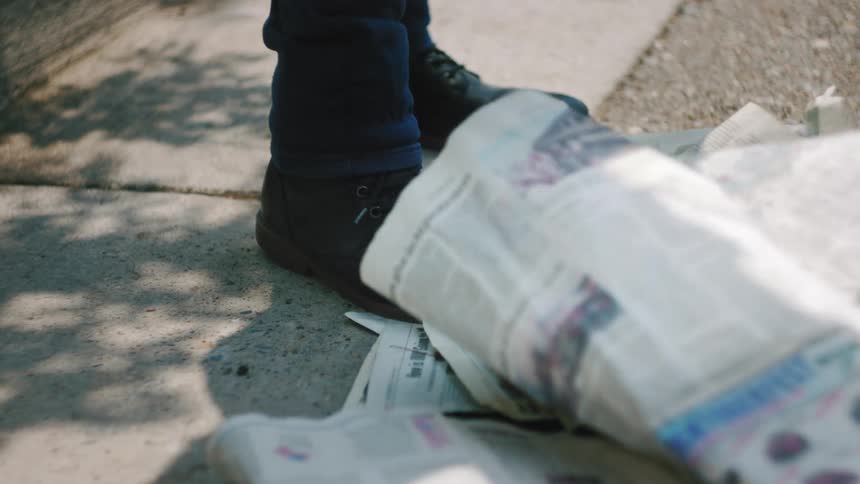 A person stands on a sidewalk with newspapers flying around them