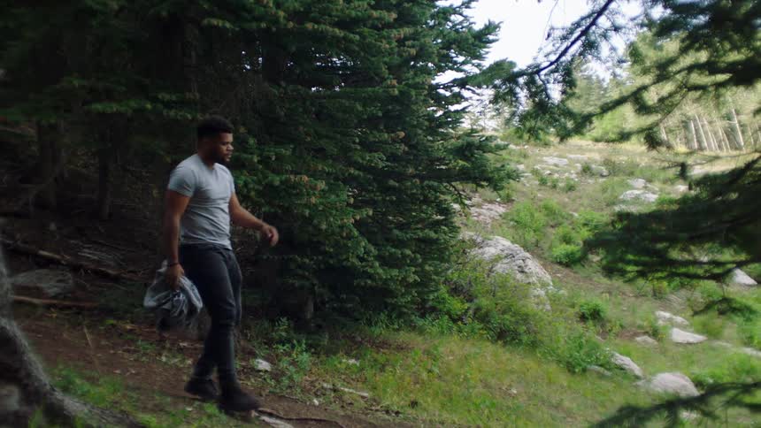 A person is walking in a forested area holding a jacket