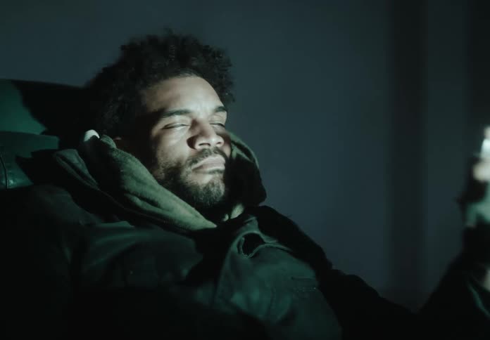 A person is reclining in a dark room holding a ring illuminated by flickering lights