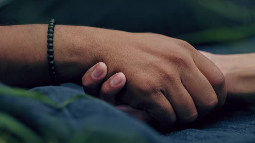 Two people holding hands with a beaded bracelet on a blue fabric
