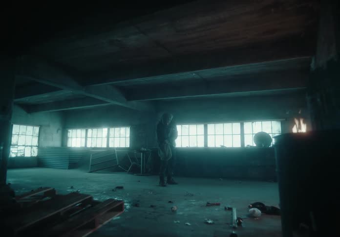 A man walks across a warehouse full of trash and debris then stops and takes something out of his pocket