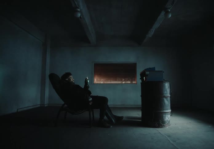 A man reclines in a chair in a room with a metal barrel in it