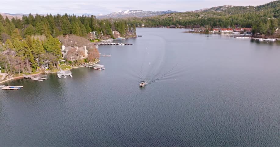 Motorboat travels through water between houses and docks occupying a forested shore on a cloudy day