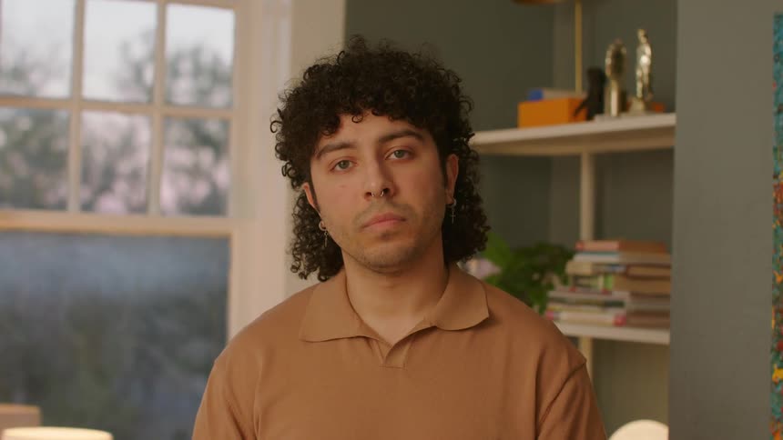 Face of a man with curly hair seated indoor at midday
