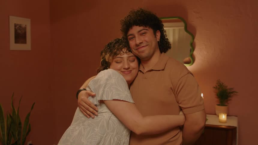 A man and a woman are standing in a room and the woman hugs the man and they are both smiling