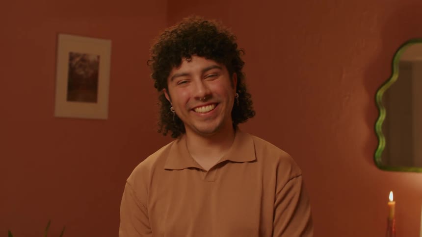 A portrait of a young man with curly hair smiling and laughing