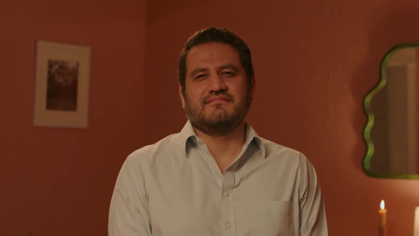 Bearded man stands in a cozy room looking at the camera
