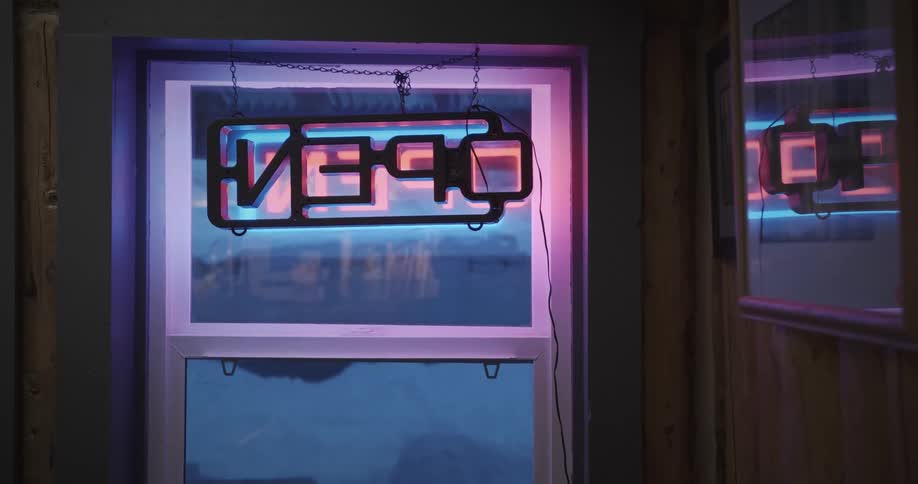 Glowing open neon sign displayed on the glass entrance door of a commercial establishment
