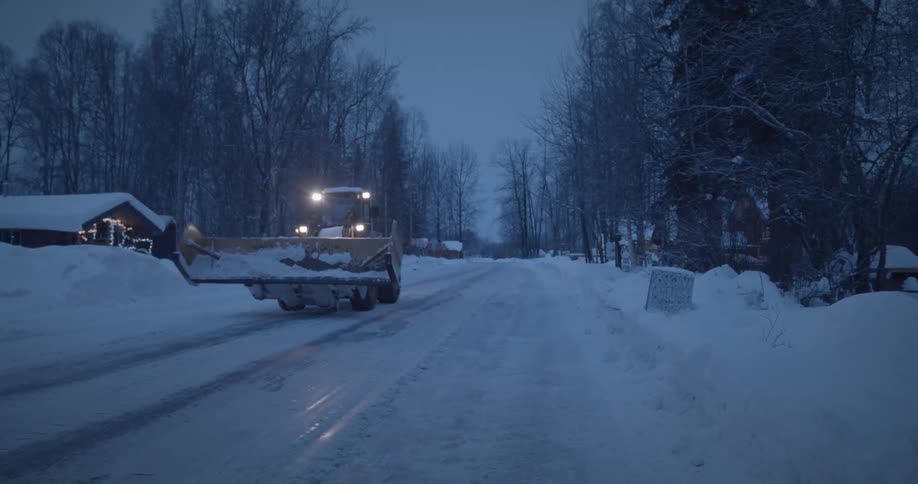 A snow plow drives down the snow filled road