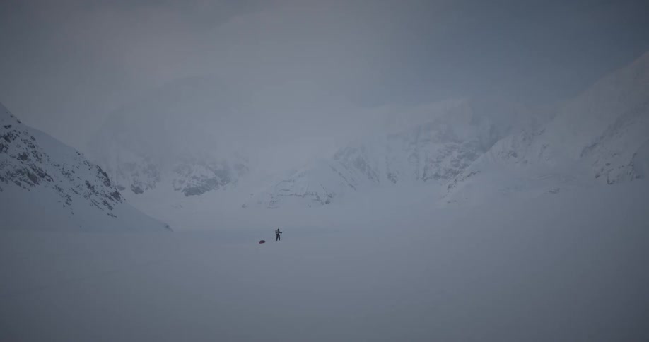 Adventurer pulls a sled through a snowy valley in the mountains