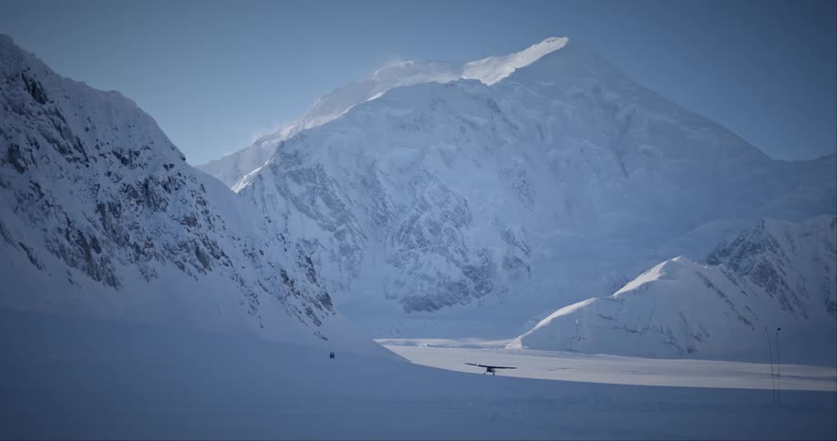A plane is landing by the snow covered mountains