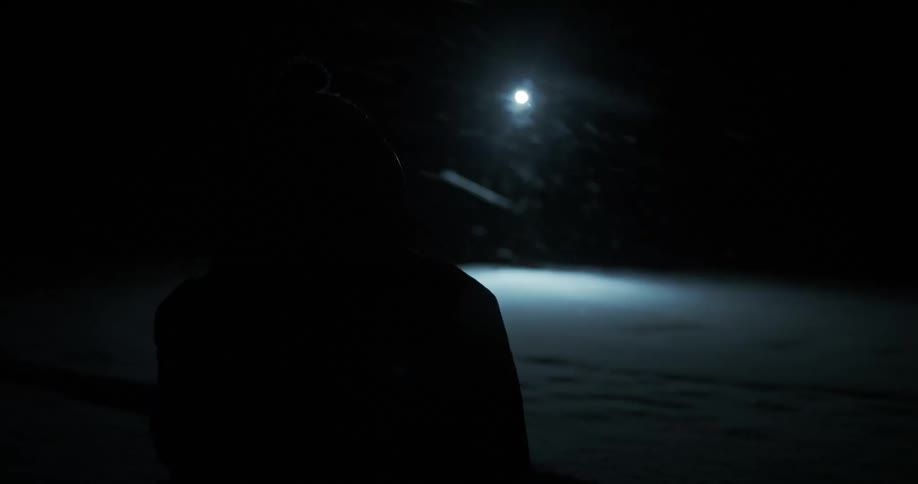 A person with a head light approaches someone during a snow storm