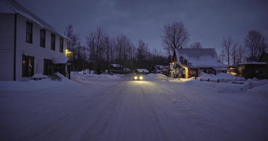 A car drives through a small town covered in snow at night