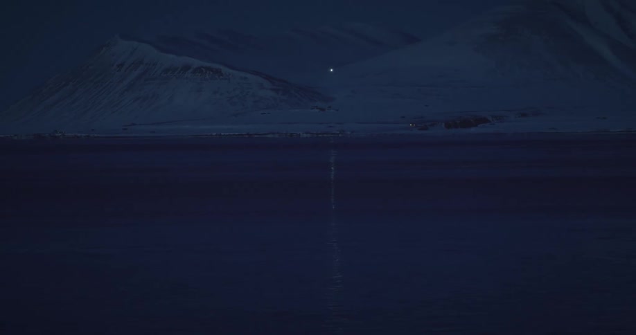 the ocean reflects the lights of a car driving down an icy mountain at night