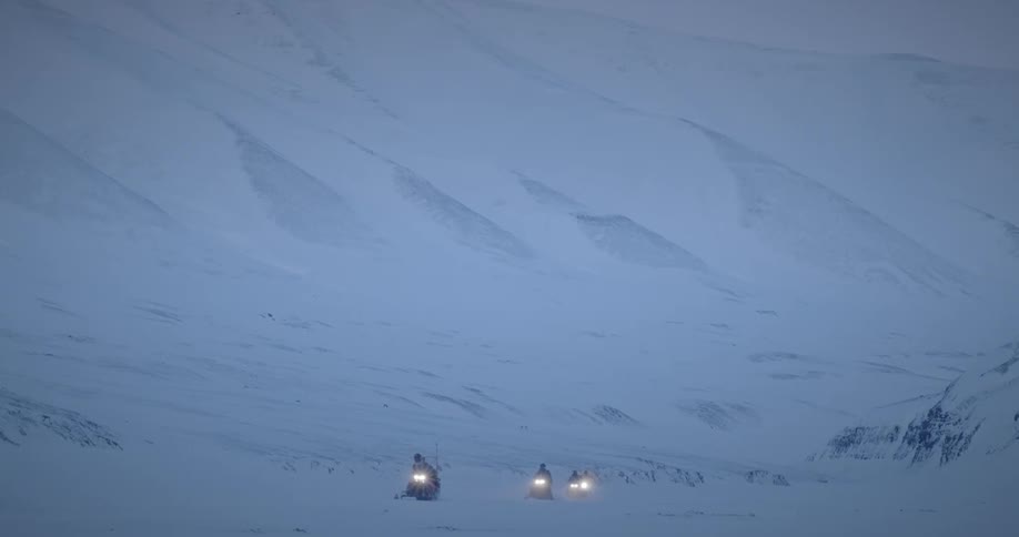 A group of people ride snowmobiles at dusk in the mountains