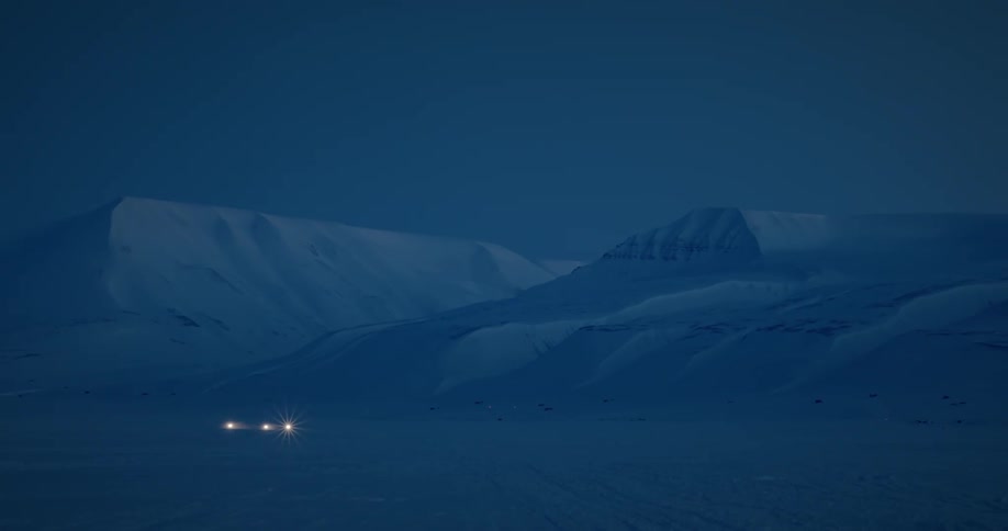 Headlights moving across a frozen mountain pass terrain at night