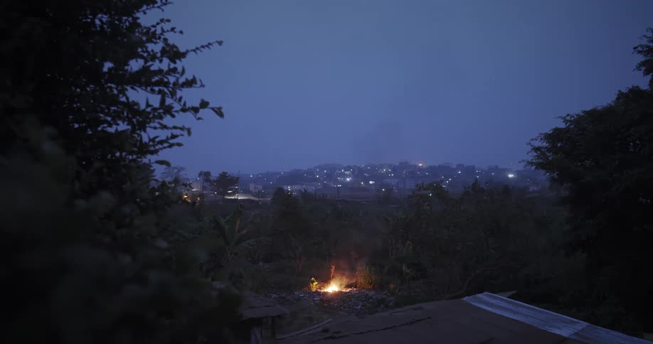 A campfire is burning on a hill far from the city