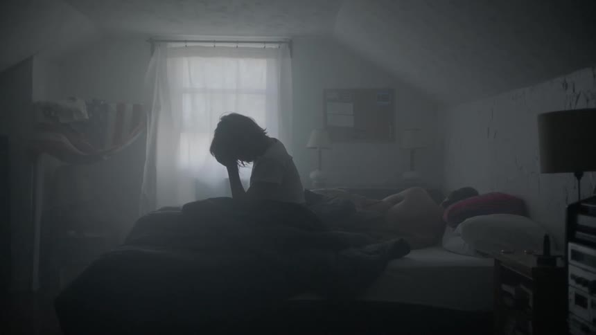A woman sits upright in bed while resting her head in her hand