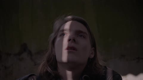 A person is sitting on the floor of a bedroom looking distressed