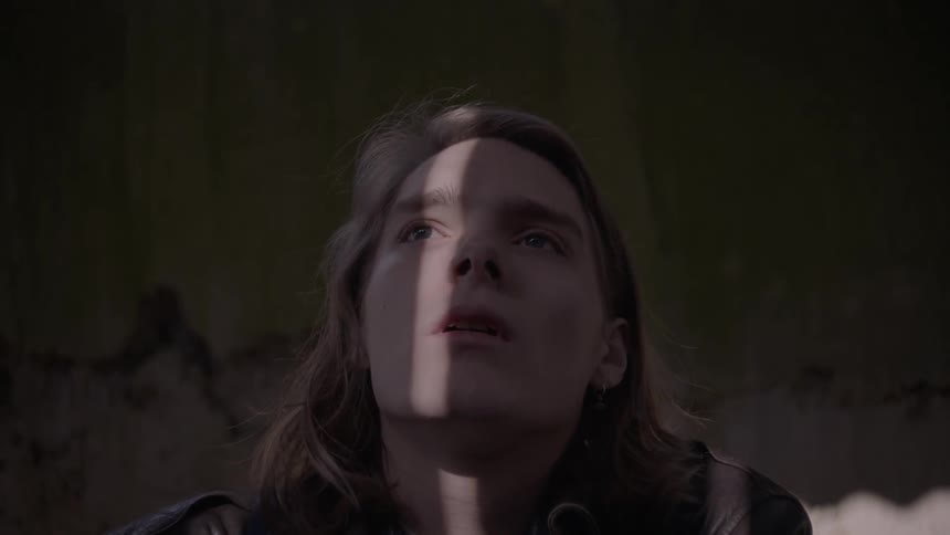 A person is sitting on the floor of a bedroom looking distressed