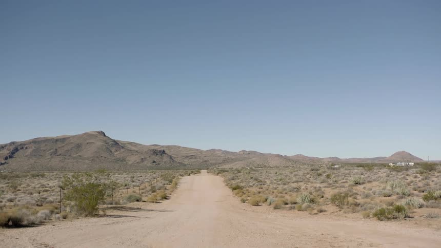 A long empty dirt road is surrounded by a desert