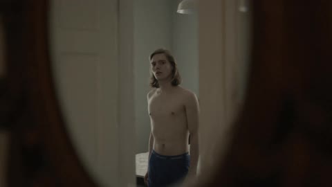 A man with long hair is staring into a mirror