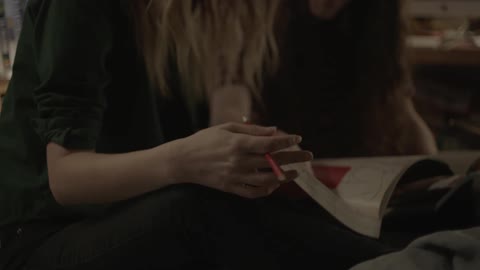 Two teenagers are sitting on interacting as they look at a book