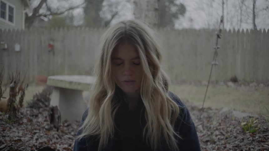 A girl is sitting in a yard and she closes and opens her eyes